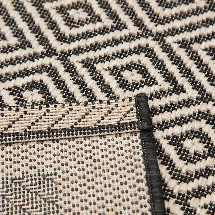 Dekoria Teppich Modern Geometric 160x230cm -  - Nahaufnahme eines gewebten schwarz-cremefarbenen Teppichs mit geometrischem Rautenmuster, das die strukturierte Rückseite zeigt.
