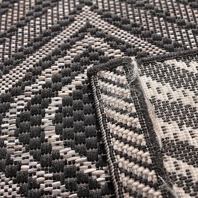 Dekoria Teppich Breeze black/ clif grey 120 x 170 cm -  - Nahaufnahme eines schwarz-weiß gemusterten Teppichs mit geometrischem Design, zeigt Webstruktur und Kante.