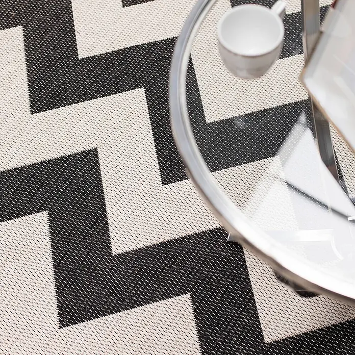 Dekoria Teppich Modern Chevron black/beige 160x230cm -  - Nahaufnahme eines schwarz-weißen Zickzack-Teppichs unter einem Glastisch mit Tasse.