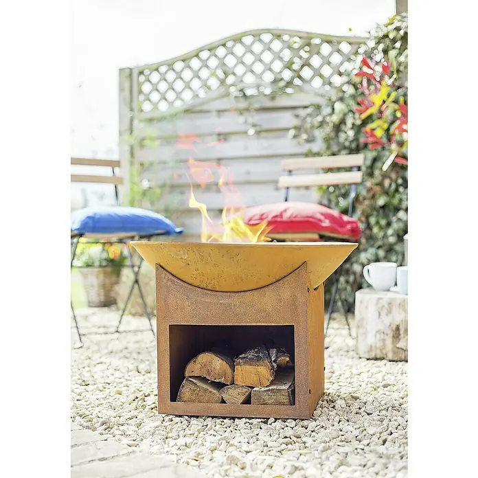 Buschbeck Feuerschale Mumbai - 56 cm, Ausstattung: Holzablagefach - Feuerstelle aus Metall mit Holz im Lagerbereich und brennendem Feuer. Ideal für gemütliche Stunden im Garten mit rustikalem Charme.