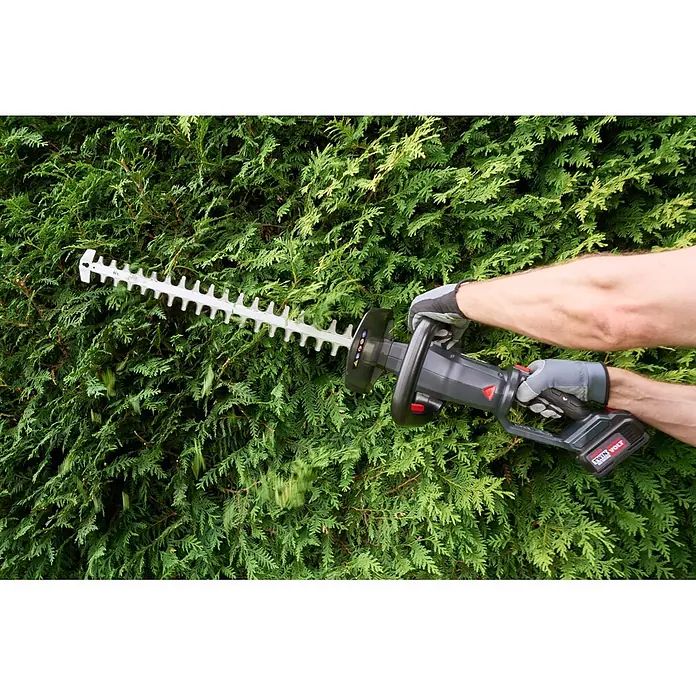 AL-KO Akku-Heckenschere HTT 3660 - 36 V, Li-Ionen, 1 Akku, Schnittlänge: 60 cm - Person trimmt eine grüne Hecke mit einer grau-schwarzen Akku-Heckenschere mit Silberklinge. 'Twin Volt' Akku sichtbar.