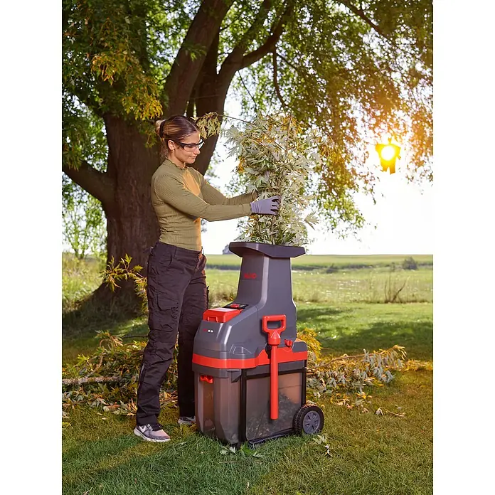 AL-KO Akku-Häcksler LH 3670 Li - Max. Aststärke: 42 mm - Eine Frau führt grüne Äste in einen grau-roten AL-KO Gartenhäcksler ein.