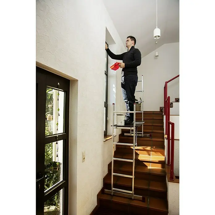Krause Corda LeitergerüstArbeitshöhe: 2,95 m - 3,75 m, Bühnengröße: 1,47 x 0,5 m, Belastbarkeit: 150 kg/m², 12 Stk. - Ein Mann steht auf einer Treppenleiter und streicht einen Fensterrahmen, mit einem Farbeimer und einem roten Farbbehälter in der Hand.