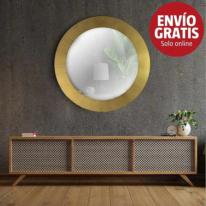Espejo de pared Circular - Diámetro: 60 cm, Oro betún - Espejo redondo con marco dorado que refleja una planta y una lámpara, colocado sobre un mueble de madera clara con puertas de rejilla.