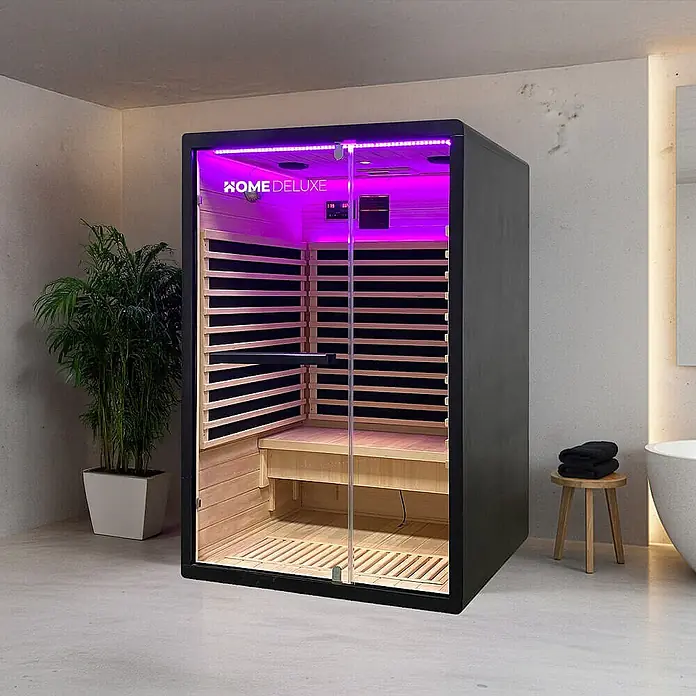 Home Deluxe Infrarotkabine NERO M Schwarz -  - Moderne Indoor-Saunakabine mit schwarzem Rahmen, Holzinterieur, Glastür und violetter LED-Beleuchtung in einem Badezimmer.