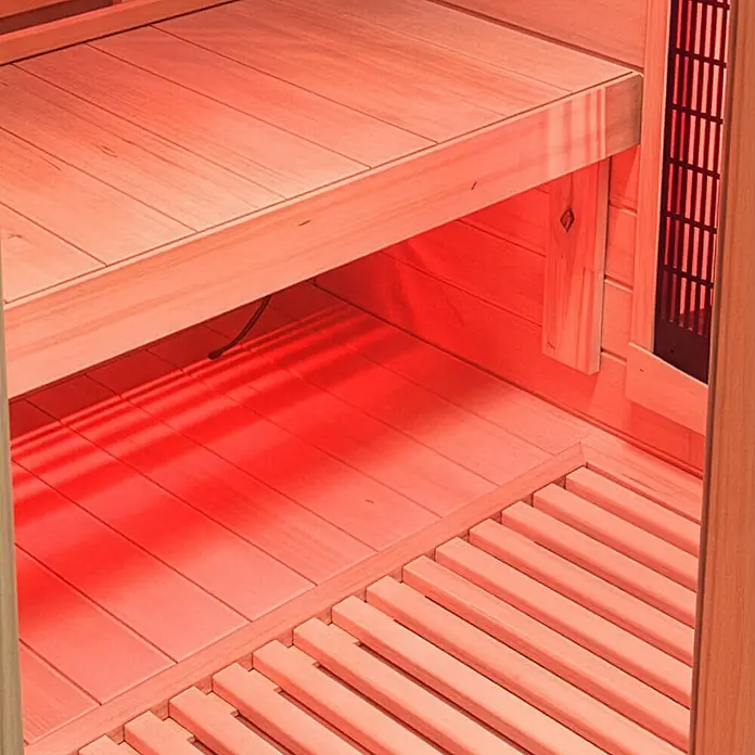 Home Deluxe Infrarotkabine SONORA M M -  - Innenansicht einer Infrarotsauna aus Holz mit rotem Leuchten der Heizelemente, Bänken und Lattenrostboden.