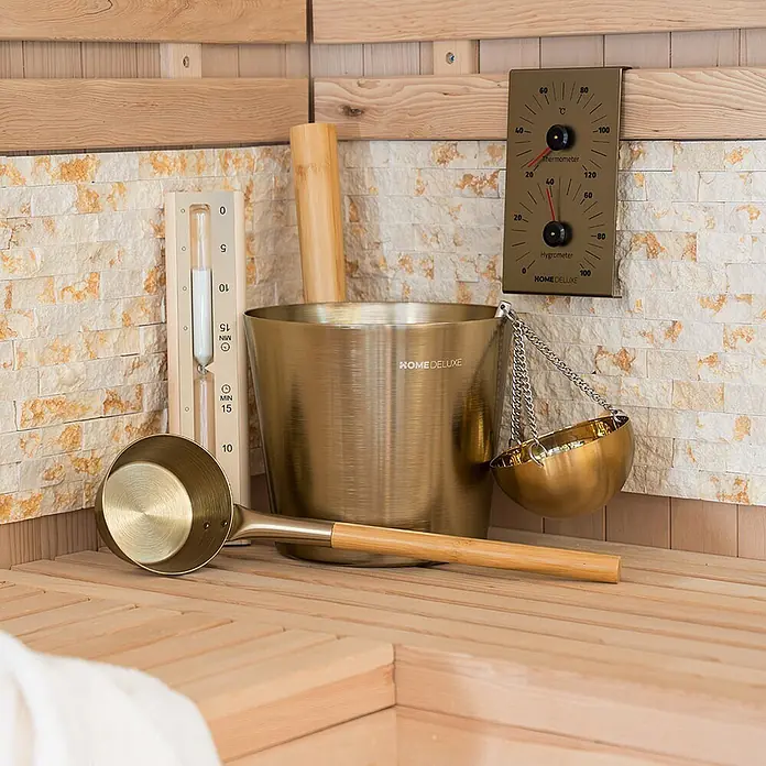 Home Deluxe Sauna-Zubehör THERA Gold -  - Bronze Saunazubehör: Eimer, Kelle, Thermometer/Hygrometer und Sanduhr, in einer Sauna arrangiert.