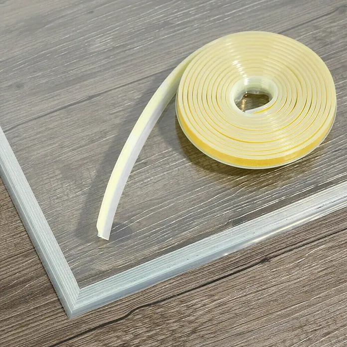 Justus Dichtlippe - Geeignet für: Glasbodenplatte, 4,5 m, Transparent - Eine Rolle Dichtungsband und ein transparentes Fensterrahmen-Set auf einem Holzboden. Perfekt zum Abdichten von Fenstern und Türen.