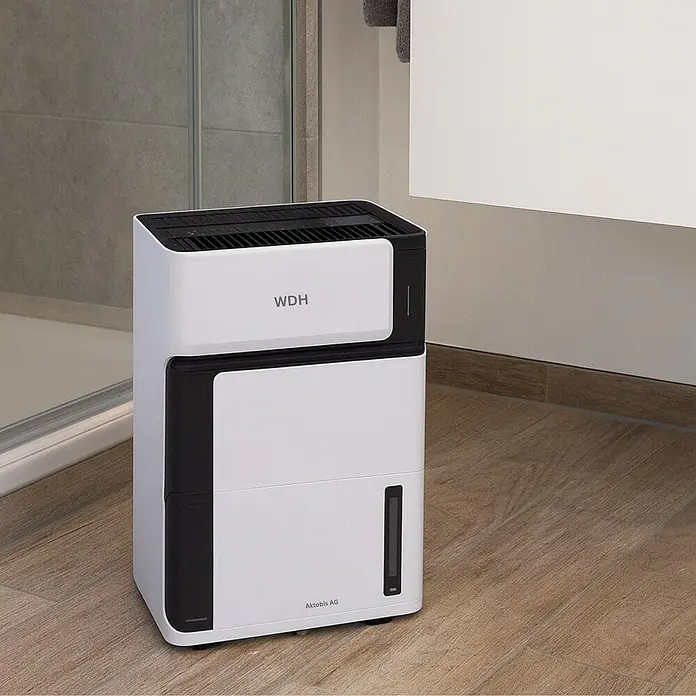 WDH Luftentfeuchter WDH-106LE - für 15m² - 8 Liter/Tag -  - Ein moderner weißer und schwarzer Luftentfeuchter steht auf einem Holzfußboden in einem Badezimmer.