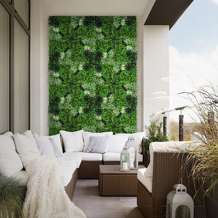 Künstliche Pflanzenwand Kunstpflanzen Wand Innen Aussen White Blossom -  - Eine künstliche grüne Wand verwandelt einen modernen Balkon, mit gemischtem Grün und helleren Akzenten, über Rattan-Gartenmöbeln.