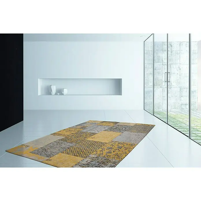 Kayoom Flachgewebeteppich Jacquard - Gold, 150 x 80 cm, 100 % Baumwolle - Ein gelb-grauer Patchwork-Teppich liegt in einem modernen, minimalistischen Raum mit großen Fenstern und eingebauten Regalen.