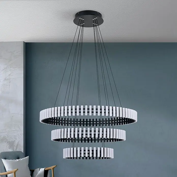 Orion Leuchten Pendlleuchte Masnion -  - Moderner dreistufiger Ring-Kronleuchter mit schwarz-weißen Elementen, in einem Raum mit strukturierter blauer Wand.