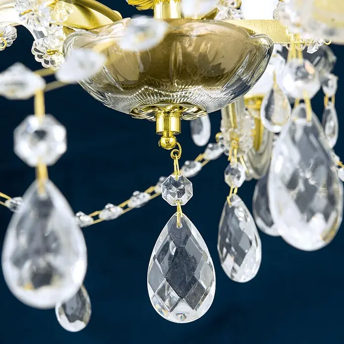 Orion Leuchten Kronleuchter Theresa Ø 56 cm -  - Nahaufnahme eines goldenen Kronleuchters mit facettierten, klaren Kristallanhängern in Tropfen- und Achteckform vor dunklem Hintergrund.