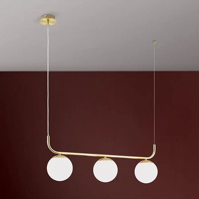 Orion Leuchten Pendelleuchte Madis -  - Eine lineare Pendelleuchte mit goldfarbenem Rahmen und drei weißen Kugelgläsern, hängt von der Decke vor einer dunklen Wand.