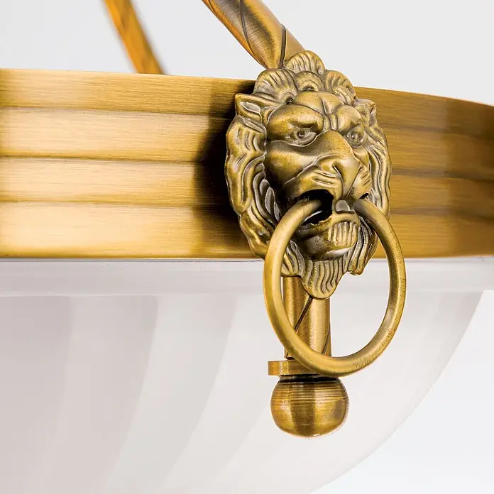 Orion Leuchten Kronleuchter Rocca -  - Verziertes Messing-Leuchtenelement mit Löwenkopfmotiv, das einen Ring hält, über einem weißen Glasdiffusor.