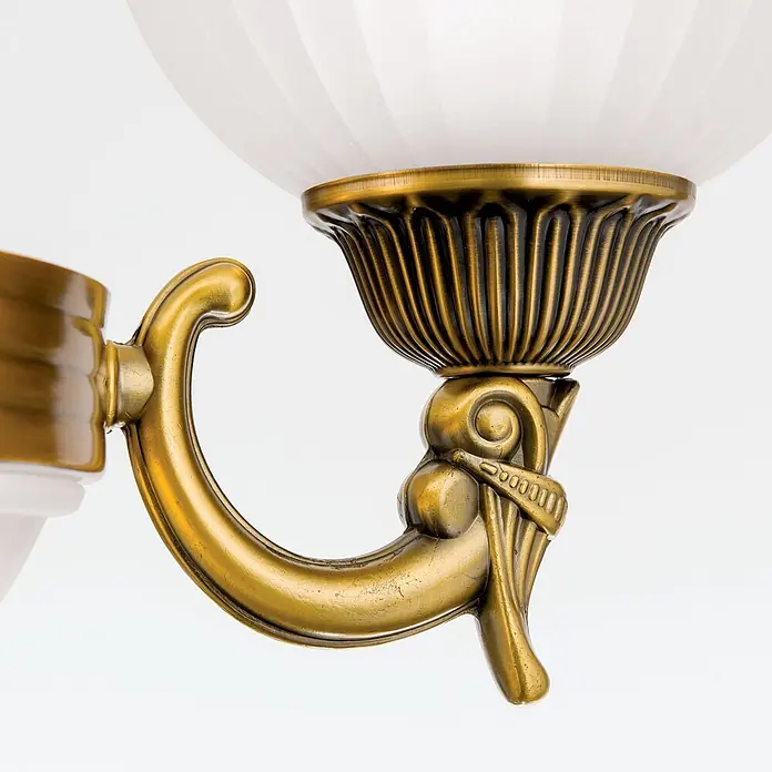 Orion Leuchten Kronleuchter Rocca -  - Detailaufnahme einer messingfarbenen Metall-Lampenfassung mit dekorativem Arm und geripptem weißem Glasschirm.