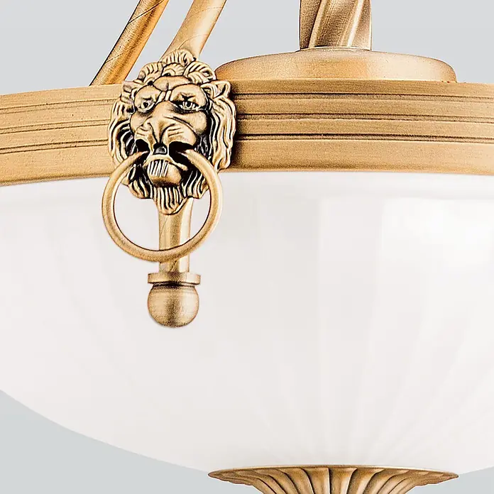 Orion Leuchten Pendelleuchte Rocca -  - Antike goldfarbene Metall-Lampenfassung mit Löwenkopfverzierung, der einen Ring hält, über einem weißen Glasschirm.