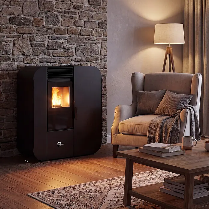 Pelletofen Slim Astral 13,8 kW Schwarz Sannover -  - Dunkelgrauer Pelletofen mit Flamme, heizt gemütliches Wohnzimmer mit Steinwand und Sessel.