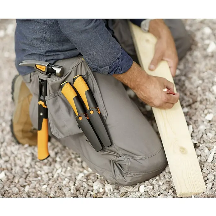 Fiskars Zimmermannsmesser - Länge: 21,5 mm - Nahaufnahme eines Mannes mit Werkzeuggürtel und Holzbrett, auf dem er mit einem Bleistift markiert.