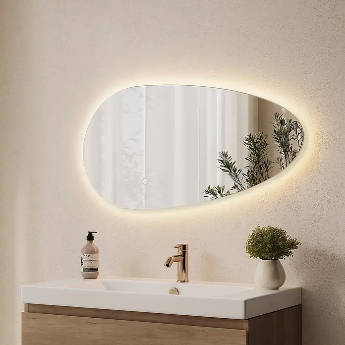 LOMAZOO LED-Badspiegel Adana asymmetrisch 80 x 40,6 cm -  - Kieselsteinförmiger LED-Spiegel mit beleuchtetem Rand, der Fenster und Pflanzen reflektiert, über einem modernen Waschbecken montiert.