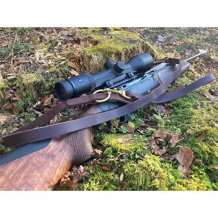 Hundeleine / Führleine - Echtleder mit Halsband – handgefertigt in Germany -  - Ein Gewehr mit Zielfernrohr und braunem Lederriemen liegt auf moosigem Boden.