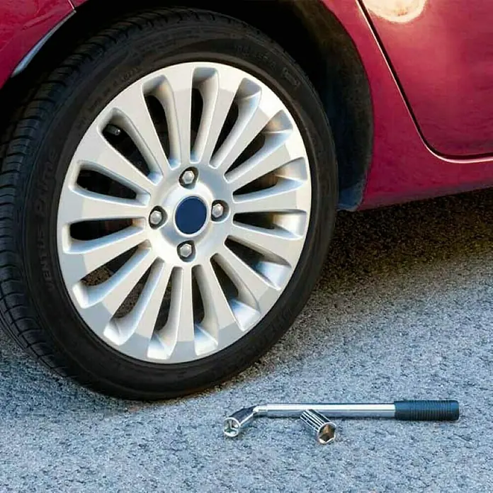 Llave de tubo - Ancho de llave: 17 mm - 19 mm - Primer plano de un cambio de neumáticos con un neumático y una llave de cruz en el suelo, centrándose en las herramientas.