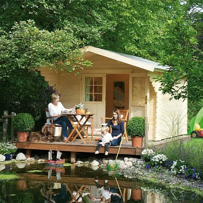 Kiehnholz Gartenhaus Helsinki - Außenmaß inkl. Dachüberstand (B x T): 340 x 443 cm, Holz, Natur - Idyllische Szene mit einem Holzgartenhaus, einer Familie und einem Teich, die das charmante Ambiente des Hauses unterstreichen.