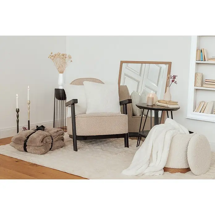 Dekokissen & Decken-Set Aimee - 2 -tlg., Weiß - Ein gemütliches Wohnzimmer mit beigem Sessel, flauschigem Teppich, Kunstpelzdecken und einer Aufbewahrungsottomane.