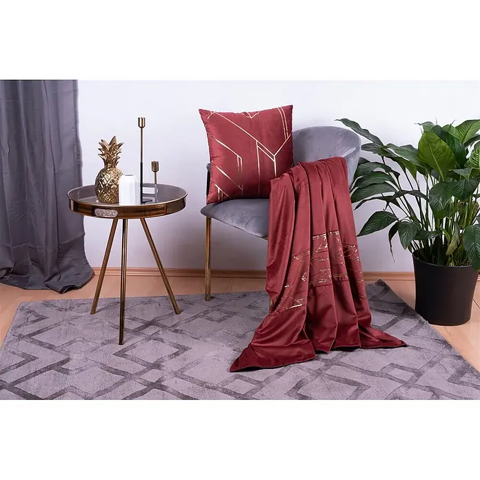 Dekokissen & Decken-Set Prisma 125 - 2 -tlg., Rot/Gold - Ein rotes Samtkissen mit goldenen geometrischen Mustern liegt auf einem grauen Stuhl, mit einer passenden Decke darüber.