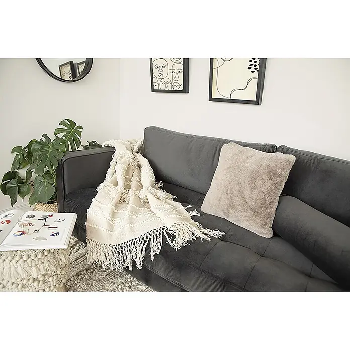 Wohndecke Bohist 325 - 130 x 170 cm, Natural, 100 % Wolle - Cremeweiße Decke mit Noppen und Fransen, über einem dunkelgrauen Sofa.