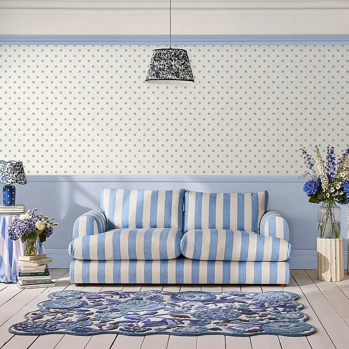 Cath Kidston Vliestapete Button Spot - Weiß/Blau - Hellblaue Polka-Dot-Tapete in einem Raum mit gestreiftem Sofa und Blumen-Teppich.