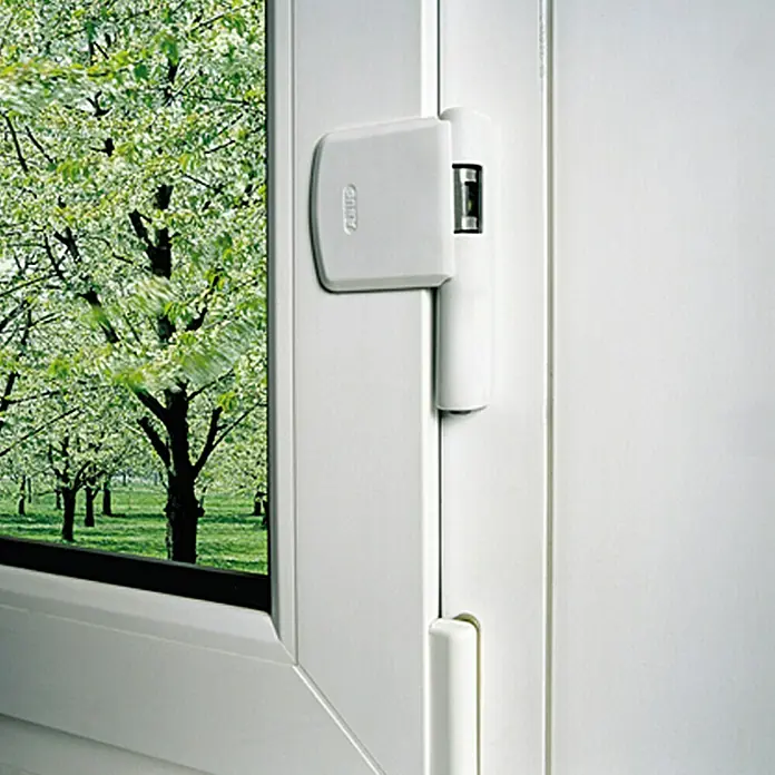 Abus Scharnierseitensicherung FAS101 - Braun - Nahaufnahme eines weißen ABUS Fensterschlosses mit Blick auf einen Garten, der Sicherheit und Ästhetik verbindet.