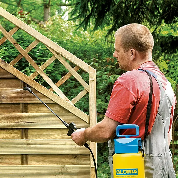 Gloria Drucksprühgerät Spray&Paint - Betriebsdruck: 3 bar, Kunststoff - Mann sprüht mit einem gelben Gloria-Drucksprüher eine Holzwand ein. Das Gerät ist ideal für Gartenarbeiten.