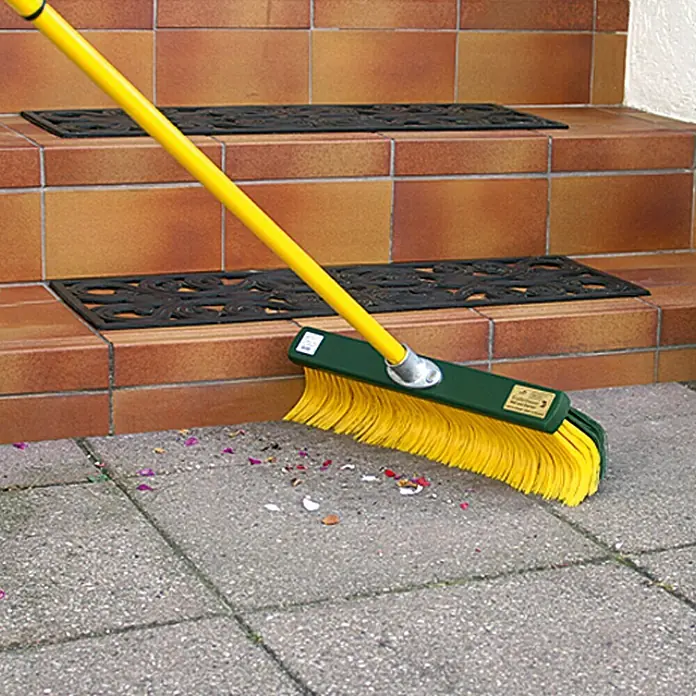 Steuber Krallenbesen - Breite: 35 cm, Einsatzbereich: Garten - Gelber Besen mit grünem Kopf, der auf einem grauen Zementboden Kehrarbeiten verrichtet.