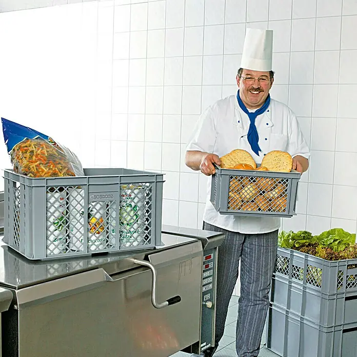 BAUHAUS Caja Euro + base con ruedas - 40 l, L x An x Al: 60 x 40 x 20 cm, 6 pzs. - Un chef en una cocina comercial sostiene una caja de pan mientras que otra caja con ingredientes está sobre una mesa de cocina.