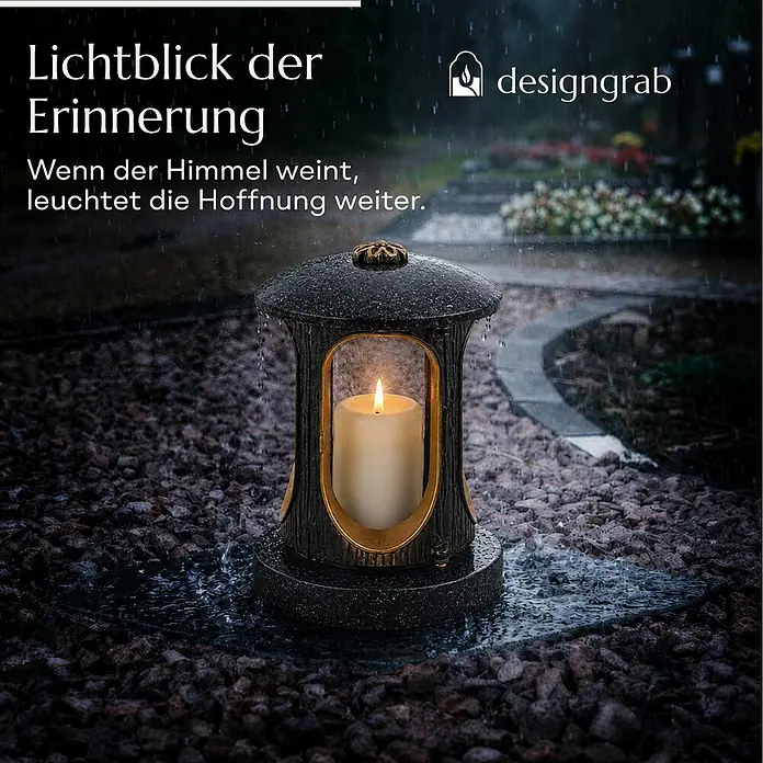 Runde Grablaterne Ø 15 cm, H 22 cm, Granit Schwedisch Schwarz, Gold-Messing -  - Dunkle Grablampe mit goldenen Akzenten und brennender Kerze, steht bei Regen auf einem Friedhofsweg.