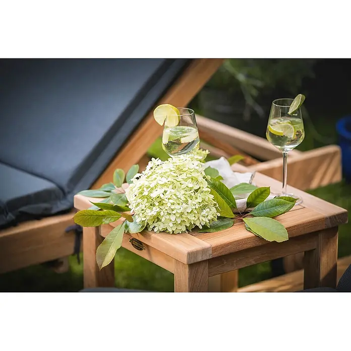 Teak Beistelltisch 40x40 cm edles Massivholz wetterfest perfekt verarbeitet -  - Teakholz-Beistelltisch im Freien neben einer Sonnenliege, mit Erfrischungsgetränken und Blumen.