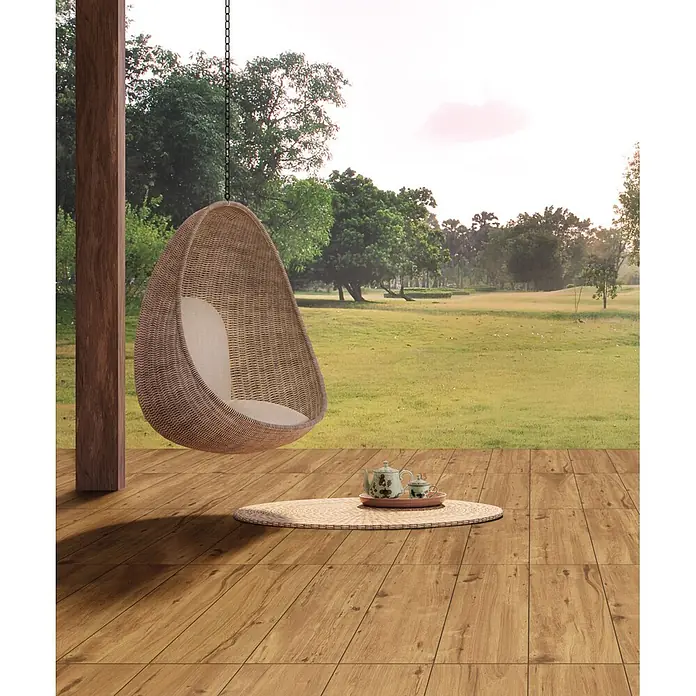 Feinsteinzeug in roher Nussbaumholzoptik 20x120, rutschhemmend -  - Rattan-Hängesessel mit hellem Kissen auf Holzterrasse mit Blick auf Naturlandschaft, bereit für Entspannung im Freien.