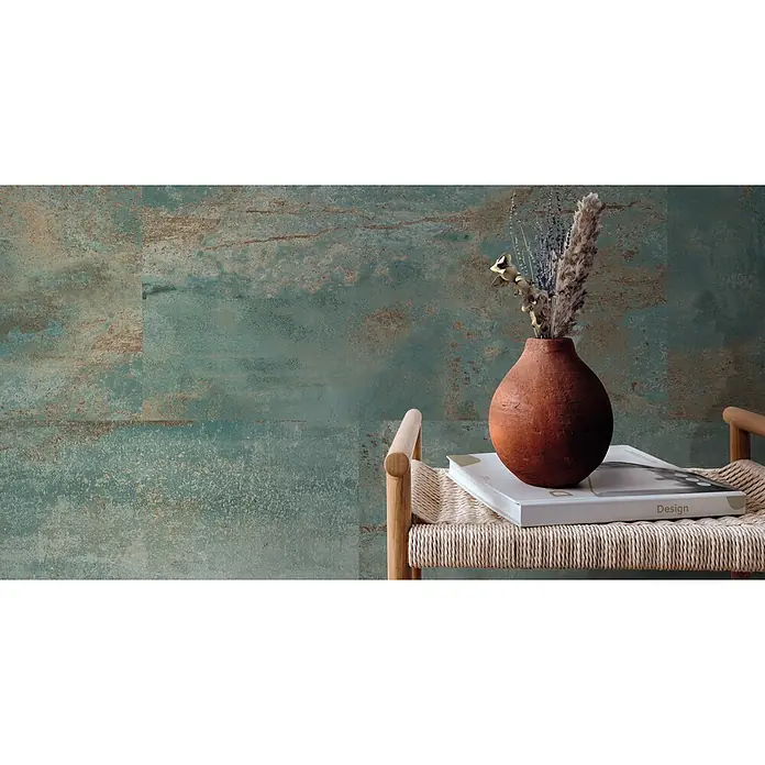 Feinsteinzeug in oxidierter grüner Metalloptik 60x120 - Ital. Fliesen -  - Türkisfarbene, distressed Wandverkleidung mit Rosttextur, hinter einem Holzstuhl mit Terrakottavase und Trockenpflanzen.