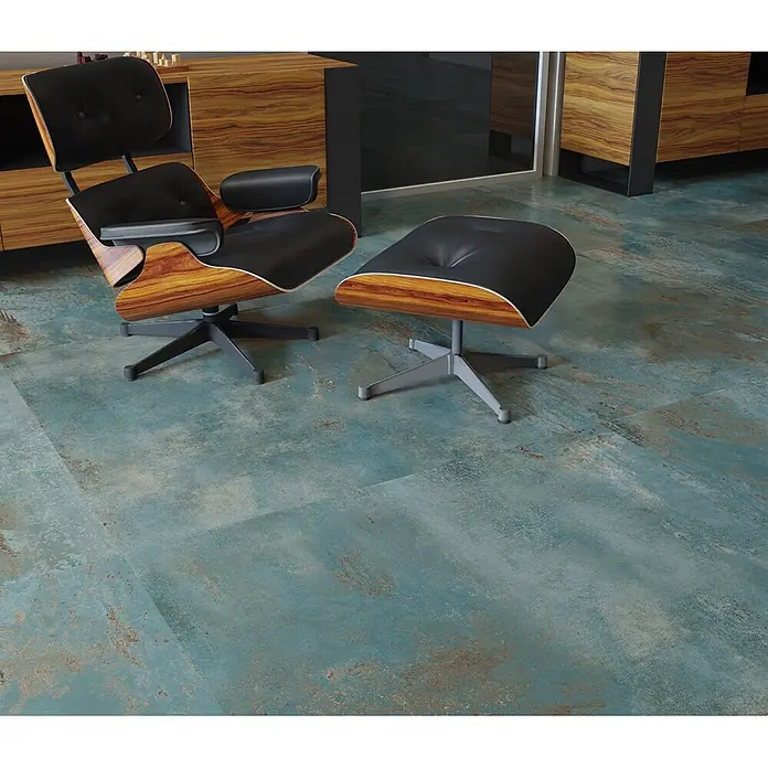 Feinsteinzeug in oxidierter grüner Metalloptik 60x120 - Ital. Fliesen -  - Schwarzer Ledersessel und passender Hocker mit Holzschalen auf teal-patinierten Bodenfliesen in modernem Wohnraum.