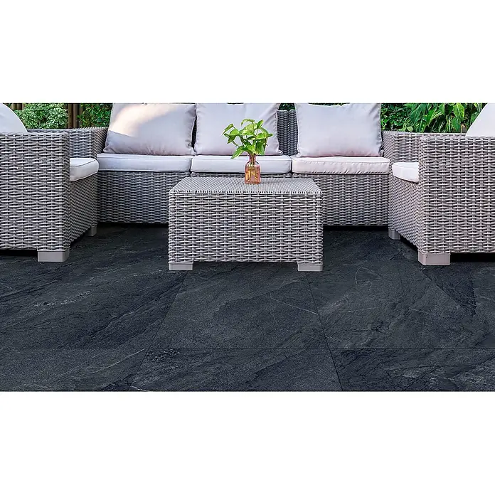 Feinsteinzeug in Jerusalem anthrazit Steinoptik 60x60 - Ital. Fliesen -  - Graues Outdoor-Sofa, Sessel und Couchtisch aus Rattan mit hellen Polstern auf dunkler Terrasse.