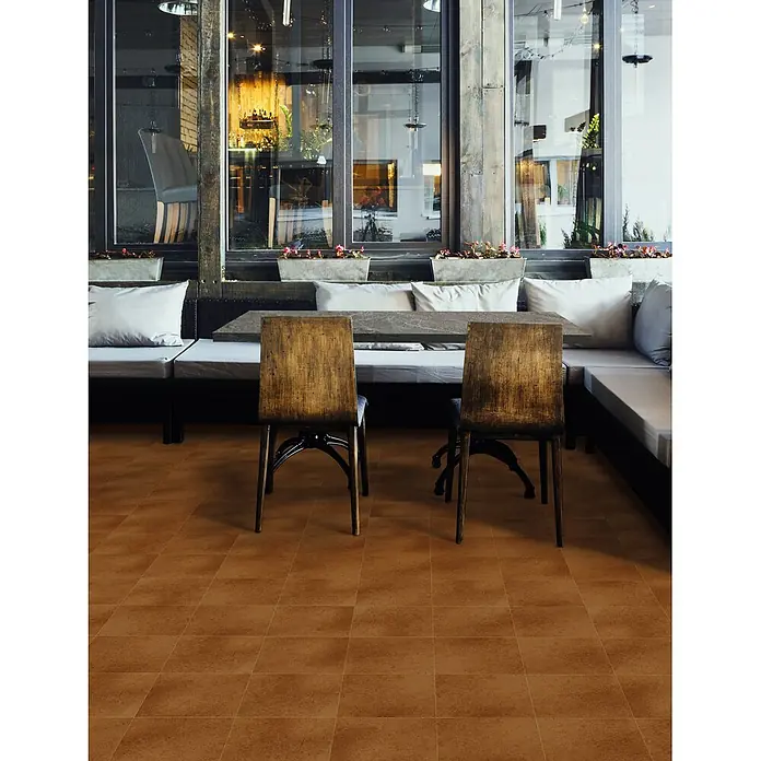 Feinsteinzeug in antiker Terrakotta natürlicher Terrakottaoptik -  - Terrakottafarbene quadratische Bodenfliesen in einem Café, unter Tischen und Stühlen verlegt.