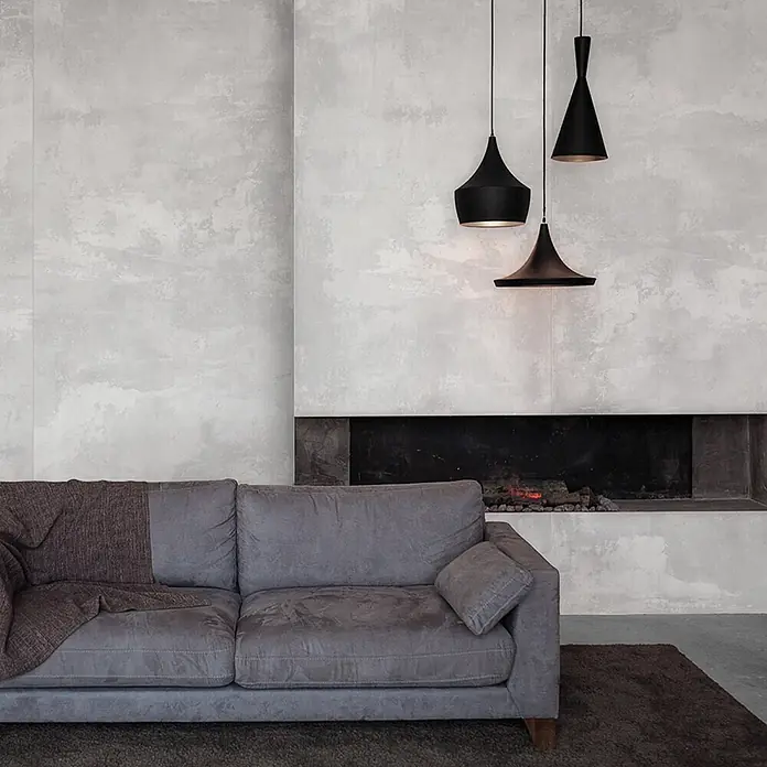 Feinsteinzeug in weißer Betonoptik 120x120 - Italienische Fliesen -  - Ein graues Stoffsofa mit einer braunen Decke steht in einem modernen Wohnzimmer neben einer strukturierten Wand und einem Kamin.