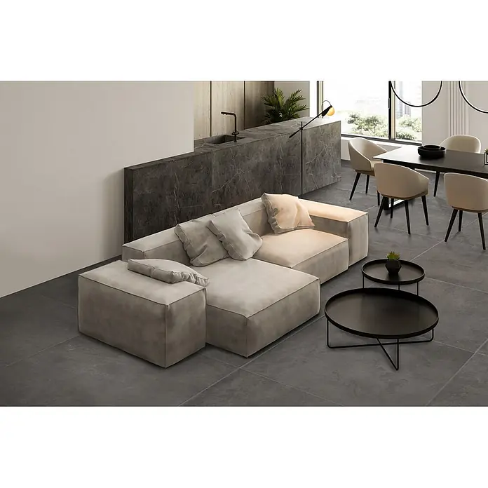 Feinsteinzeug in gewachster anthrazitfarbener Betonoptik 120x120 -  - Modernes offenes Wohnzimmer mit hellgrauem Ecksofa, dunkelgrauer Kücheninsel aus Stein und schwarzem Esstisch mit beigen Stühlen.
