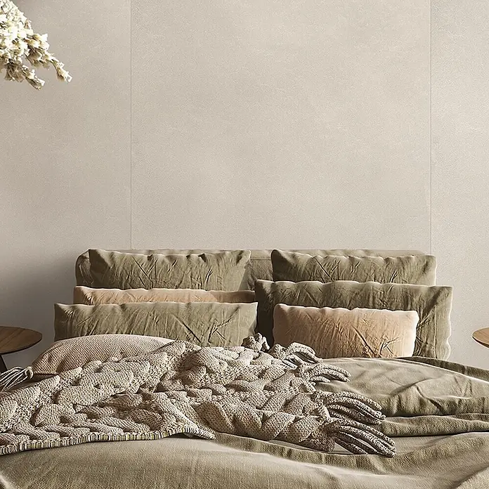 Feinsteinzeug in farbiger weißer Betonoptik 60x60 - Italienische Fliesen -  - Ein Bett mit verschiedenen grünen und beigefarbenen Samtkissen und einer strukturierten, grob gestrickten Decke.