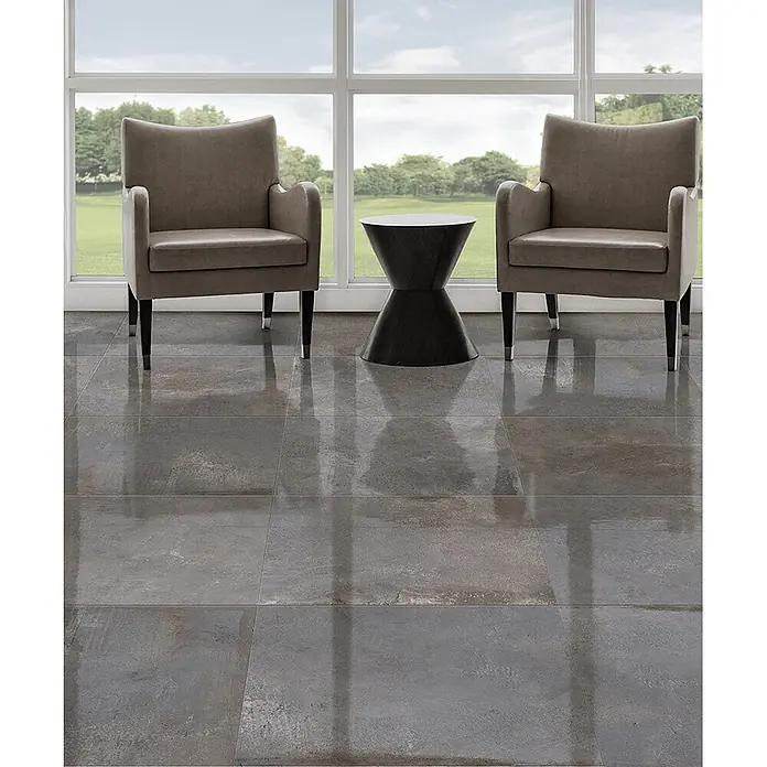 Feinsteinzeug in metallischer dunkelgrauer Betonoptik 60x120 -  - Glänzende, graue, texturierte Bodenfliesen in einem modernen Raum mit Sesseln und Tisch, die Licht reflektieren.