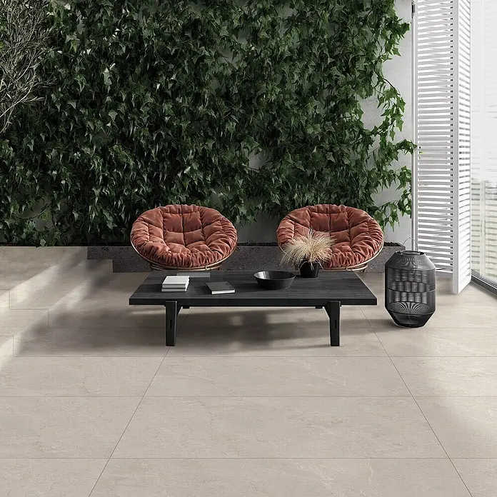 Feinsteinzeug in weißer Steinoptik 60x90, 20 mm, rutschhemmend -  - Eine einladende Außenterrasse mit hellem beigem Boden, zwei rostfarbenen Stühlen und einem schwarzen Couchtisch.