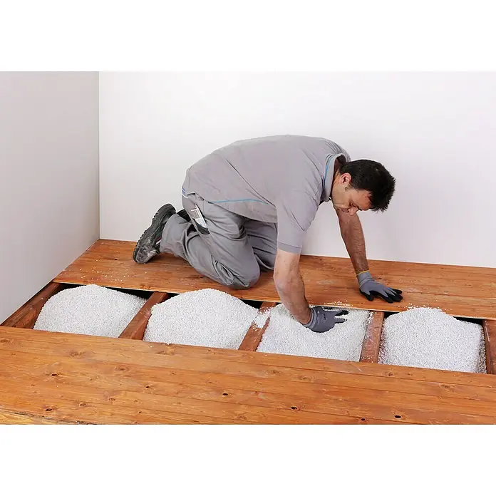 Knauf Isoself Hohlraumdämmung - 100 l - Ein Handwerker kniet auf einem Holzboden und füllt die Zwischenräume mit weißen Dämmstoffgranulaten, um die Wärmeisolierung zu verbessern.