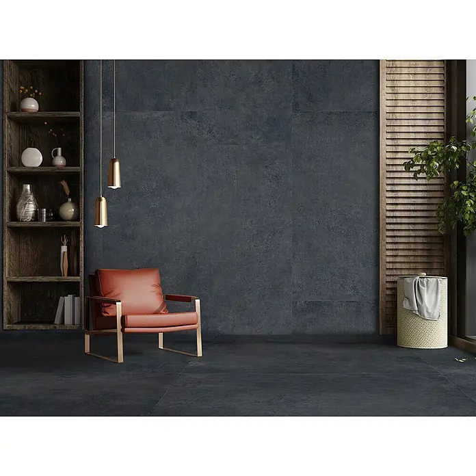 Feinsteinzeug in moderner schwarzer Betonoptik 80x80 - Italienische Fliesen -  - Ein modernes Zimmer mit großen dunkelgrauen Fliesen in Betonoptik an Wänden und Boden, ergänzt durch einen orangefarbenen Sessel und ein Holzregal.