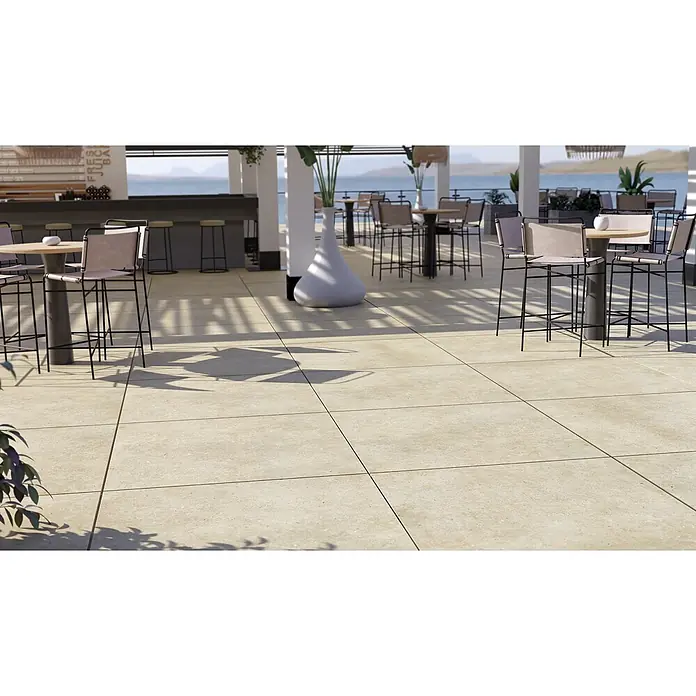 Feinsteinzeug in beiger Betonoptik 60x60, rutschhemmend - Ital. Fliesen -  - Hellfarbene Outdoor-Pflasterfliesen auf einer Bartterrasse mit Tischen und Meerblick.